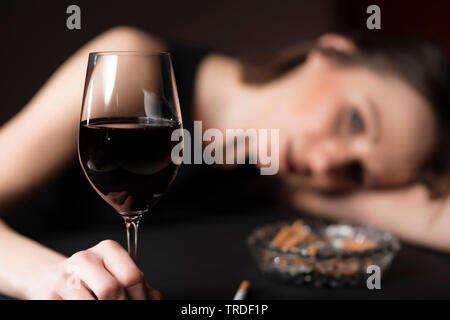 Portrait d'un déprimé et femme désalcoolisée tenant un verre de vin avec des cigarettes en face d'elle Banque D'Images