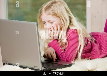 Portrait d'une fille allongée sur le sol et jouer avec un ordinateur portable Banque D'Images