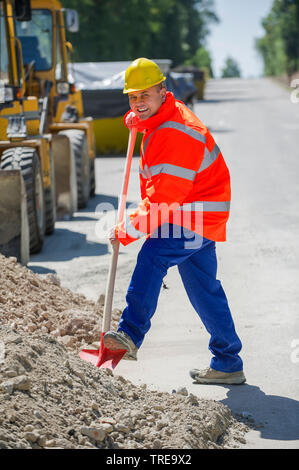 Travailleur de la construction d'une veste haute visibilité orange, pelleter du sable sur une route Banque D'Images
