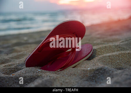 Tongs sur la plage de sable de plage avec le coucher du soleil et de l'océan en arrière-plan de la mer Banque D'Images