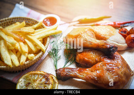 Cuisses de poulet rôties sur planche à découper en bois et de frites panier avec citron maïs chili épicé épices herbes et tomate sur table à manger nourriture / grill Banque D'Images