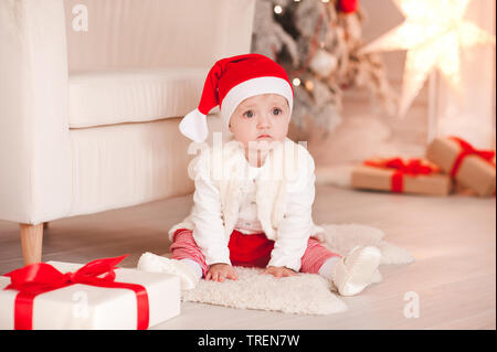 Triste petite fille 1 ans wearng santa claus hat sitting on floor sur fond de Noël dans la chambre. Ouvrir des cadeaux. Saison de vacances. Banque D'Images