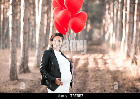 Smiling pregnant woman holding ballons en forme de coeur à l'extérieur. En regardant la caméra. La maternité. La maternité. Banque D'Images