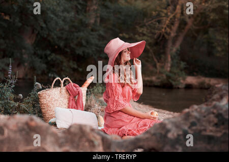 Smiling girl wearing élégant robe rose et chapeau. Pique-nique en plein air. 20s. Banque D'Images