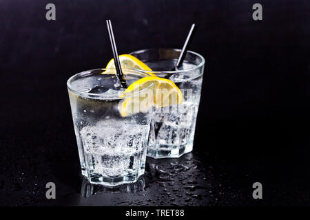 Deux verres d'eau gazeuse fraîche avec des glaçons et des rondelles de citron. L'eau de soude sur fond noir. Banque D'Images