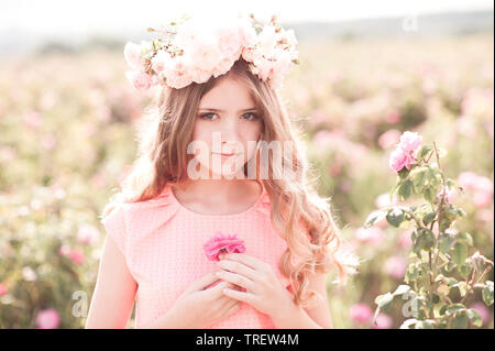 Teen blonde girl wearing wreath avec des roses à l'extérieur. Holding flower. En regardant la caméra. La Romance. Banque D'Images