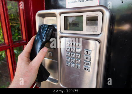 Personne soulevant le combiné et se préparer à composer un numéro / Numérotation à partir d'un modèle tardif téléphone public à pièces / payphone payer téléphone dans un original rouge / call box. England UK Banque D'Images