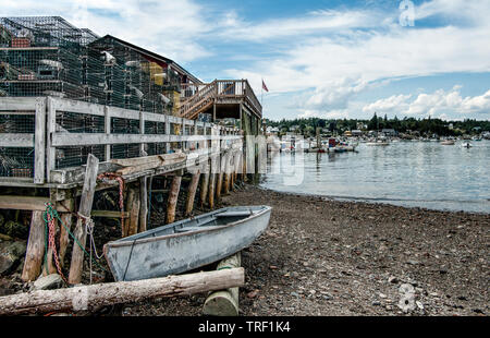 Port de pêche de la Nouvelle Angleterre : un petit bateau attend à côté d'une jetée en bois empilées de casiers à homard sur une baie dans le sud-est du Maine. Banque D'Images