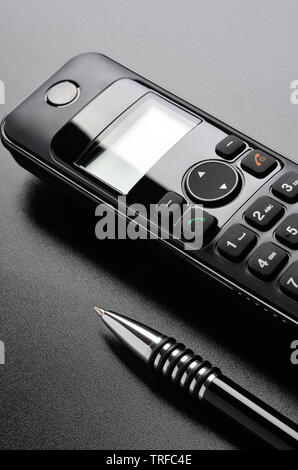 Téléphone et stylo à bille sur la surface grainé noir Banque D'Images