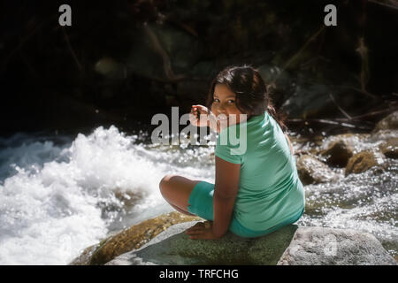 Jeune fille assise sur un rocher à côté de river rapids pendant un camp d'excursion d'une journée. Banque D'Images