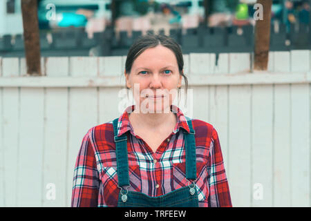 Femme sérieuse farmer posing on ferme. Woman farm worker wearing plaid shirt et jeans salopettes looking at camera. Banque D'Images