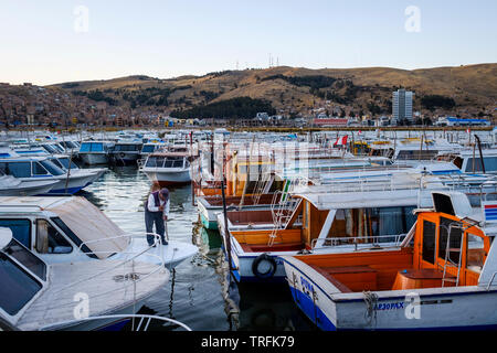 Boatkeeper travaille sur l'boats docked in le soir sur Muelle lacustre au Port de Puno sur le lac Titicaca Puno avec en arrière-plan, Pérou Banque D'Images