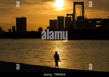 Une femme, en silhouette, bénéficie de la vue sur Rainbow Bridge depuis une plage à Odaiba, Tokyo, Japon. Banque D'Images