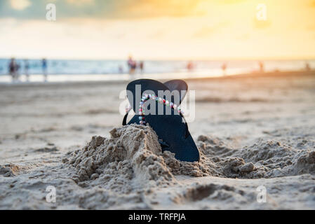 Tongs sur la plage de sable de plage avec le coucher du soleil et de l'océan en arrière-plan de la mer Banque D'Images