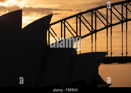 L'Opéra de Sydney et le Harbour Bridge en silhouette avec orange un ciel du soir. Les marcheurs pont peut être vu grimper sur le pont. Banque D'Images