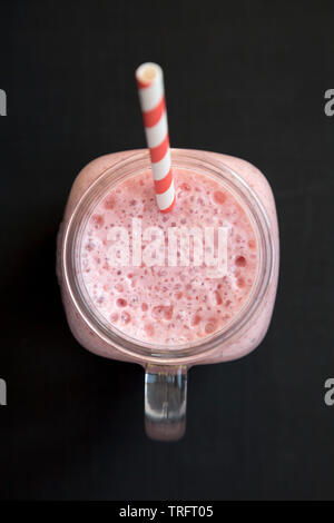 Smoothie fraise banane dans un bocal en verre mug sur fond noir, vue du dessus. Les frais généraux, de dessus, de mise à plat. Close-up. Banque D'Images