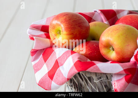 Les pommes, de variétés, de jazz sur tissu vichy dans un panier en osier trug. Sur un fond de bois blanc. Banque D'Images