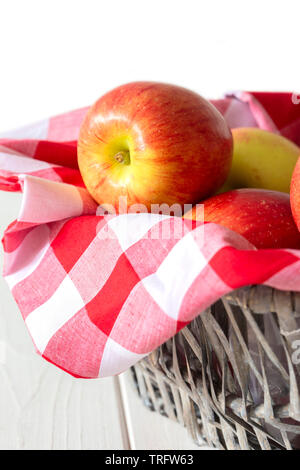 Les pommes, de variétés, de jazz sur tissu vichy dans un panier en osier trug. Sur un fond de bois blanc. Banque D'Images