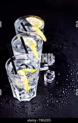 Trois verres avec de l'eau gazéifiée froide avec les tranches de citron et des glaçons libre. L'eau de soude sur backgroundwith noir copie espace.