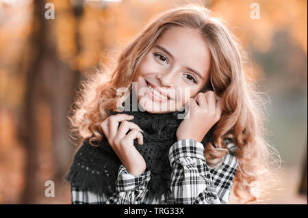 Automne portrait of smiling teen blonde Fille 13-14 ans portant foulard tricoté posant plus de feuilles jaunes à l'extérieur. En regardant la caméra. Adolescent capot. Banque D'Images