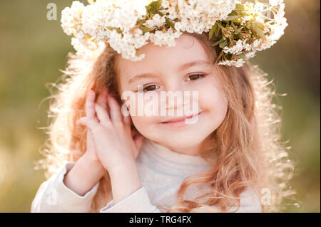 Sourire petite fille 4-5 ans portant bandeau de fleurs sous le soleil de la lumière à l'extérieur. Portrait d'été de l'enfant. Poser sur la nature de fond vert. Banque D'Images