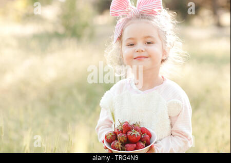 Sourire petite fille 4-5 ans holding bowl avec des baies à l'extérieur. En regardant la caméra. Banque D'Images