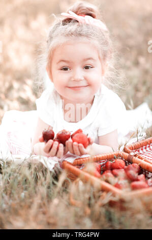 Sourire petite fille 4-5 ans couché avec panier de fraises à l'extérieur. En regardant la caméra. L'enfance. La saison d'été. Banque D'Images