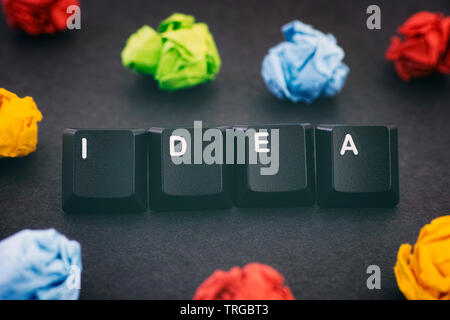 Idée. Le mot idée sur un fond noir avec des boules de papier froissé colorés autour de lui. Close up. Banque D'Images