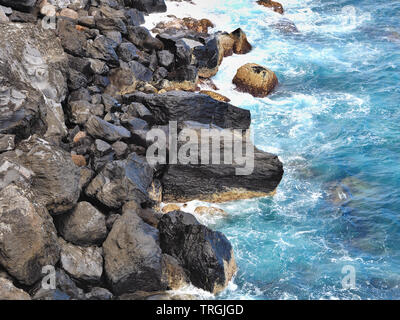 Pierres naturelles de lave noire qui brille, la côte sauvage dans le nord de Tenerife, en face d'elle une couleur bleu-vert, le tout dans l'Atlantique close-up Banque D'Images