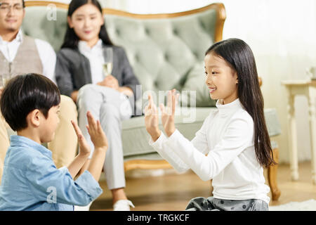 Deux enfants asiatiques mignon petit frère et sœur assis sur un tapis de jeu jouer avec parent assis sur un canapé à l'arrière-plan Banque D'Images