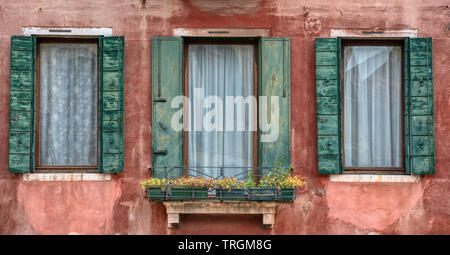 Photographie prise de trois érodés, peint vert windows contre un mur de plâtre texturé rouge pâle dans l'eau ville médiévale de Venise, Italie. Banque D'Images