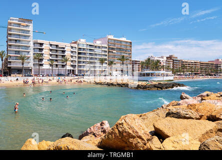 Torrevieja, Espagne- 16 mai 2019 : Playa Del Cura Orihuela Costa Resort city, waterside afficher les personnes bronzer nager dans la baie turquoise de l'eau dans la mer Méditerranée Banque D'Images