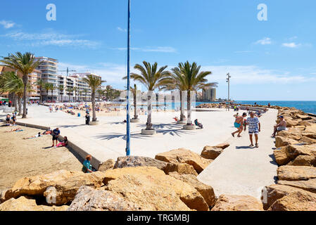 Torrevieja, Espagne - 16 mai 2019 : Beaucoup de gens touristes marcher sur la promenade bordée de palmiers en bord de piscine bains de soleil au repos sur la plage de Playa Del Cura Banque D'Images