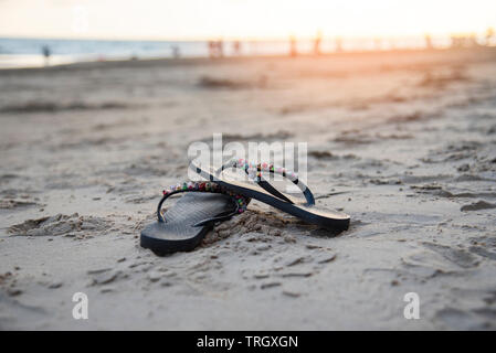 Tongs sur la plage de sable de plage avec le coucher du soleil et de l'océan en arrière-plan de la mer Banque D'Images