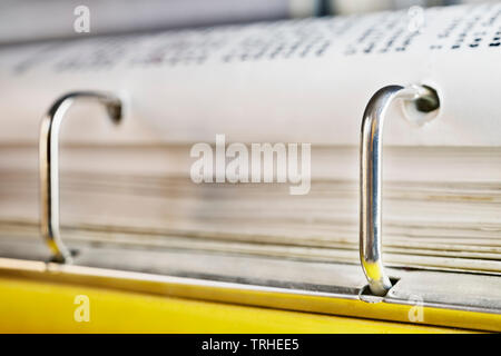 Classeur jaune ouvert close up , pile de livres blancs et d'anneaux en métal brillant , dans l'arrière-plan noir out of focus Banque D'Images