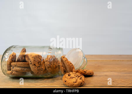 Pot en verre avec des cookies aux pépites de chocolat de son côté. Les cookies du pot sur la table en bois. Fond blanc Banque D'Images