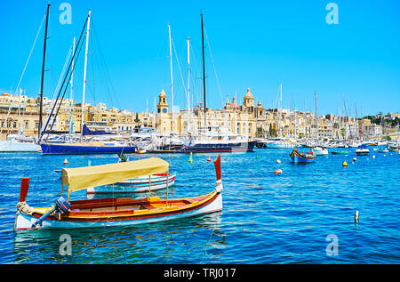 Le solitaire luzzu voile en face de la marina de yachts amarrés de Vittoriosa et médiévale Birgu sur la rive opposée, à Malte. Banque D'Images