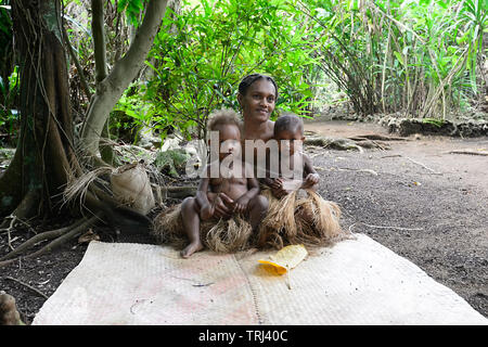 Jeune mère Tribal assis sur le sol avec deux bambins portant des jupes, Pepeyo herbe traditionnelle Cultural Village, Port Vila, l'île d'Efate, Vanuat Banque D'Images