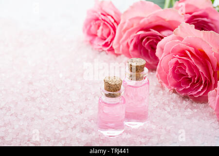 Deux bouteilles avec de l'huile de rose, spa des cristaux de sel et de roses roses. Banque D'Images