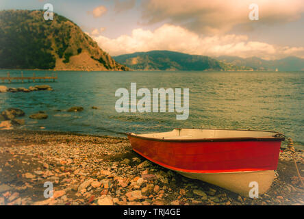 Un seul bateau à rames sur un rivage rocailleux avec un fond de mer et falaises. Il y a un classement de couleur appliquée à cette photo. Banque D'Images