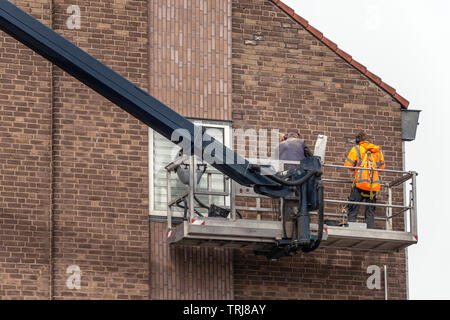 Les travailleurs de la construction sont debout sur une plate-forme d'une grue machines près d'un mur d'un appartement Banque D'Images