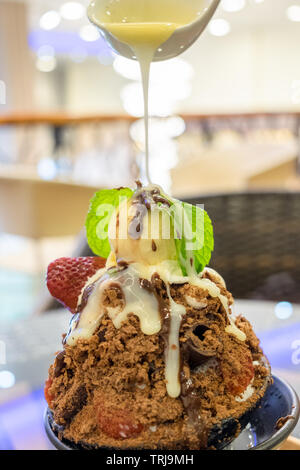 Verser le lait concentré sur le dessert au chocolat et fruits bingsu Banque D'Images