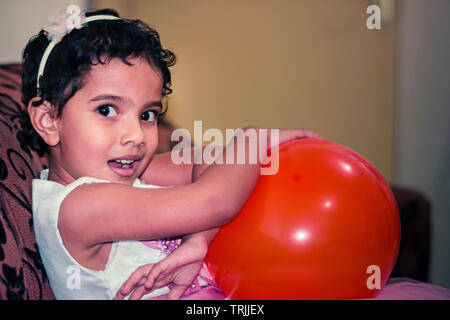 Dubai, UAE - 20 août 2018 : un mignon petit excité Indian girl sitting on sofa holding et un ballon rouge Banque D'Images