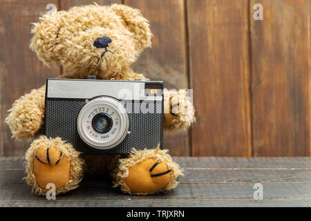 Ours en peluche brun holding old retro photo caméra sur fond de bois Banque D'Images