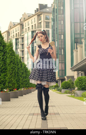 Jolie jeune femme avec des bonbons en robe noire marche sur street Banque D'Images