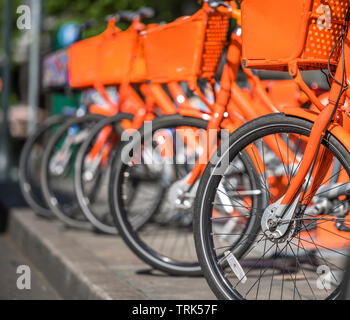 Transport des vélos de rue (orange avec panier de biens pour voyager autour de la ville dans la rangée stand sur réseau de location de stationnement en attente de Banque D'Images