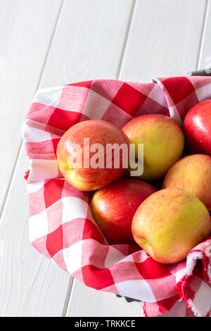 Les pommes, de variétés, de jazz sur tissu vichy dans un panier en osier trug. Sur un fond de bois blanc. Banque D'Images