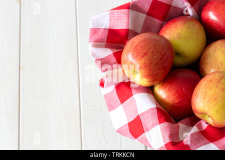 Les pommes, de variétés, de jazz sur tissu vichy dans un panier en osier trug. Sur un fond de bois blanc. Banque D'Images