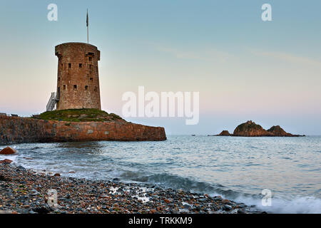 Image de la tour de Jersey, Jersey, la HOCQ Michaël Mobilis in Mobile au coucher du soleil avec des petites vagues et des pierres sur la plage. Banque D'Images