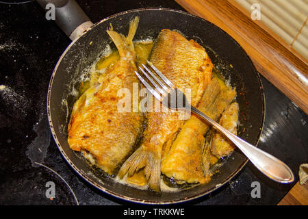 La photo de l'ensemble du poisson frit sans tête sur le gril ou la poêle avec une fourchette sur la cuisinière électrique Banque D'Images